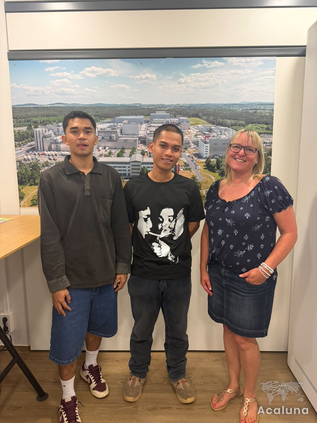 Two apprentices with their training supervisor in front of a photo of their production site